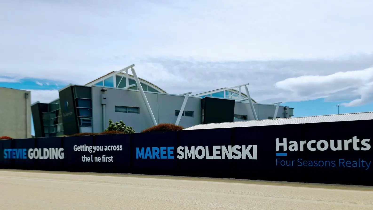 Temporary hoardings installation for Harcourts Real Estate along a walkway at a racecourse. Hoardings are a durable and impactful temporary or permanent signage option for fencing and building exteriors. 