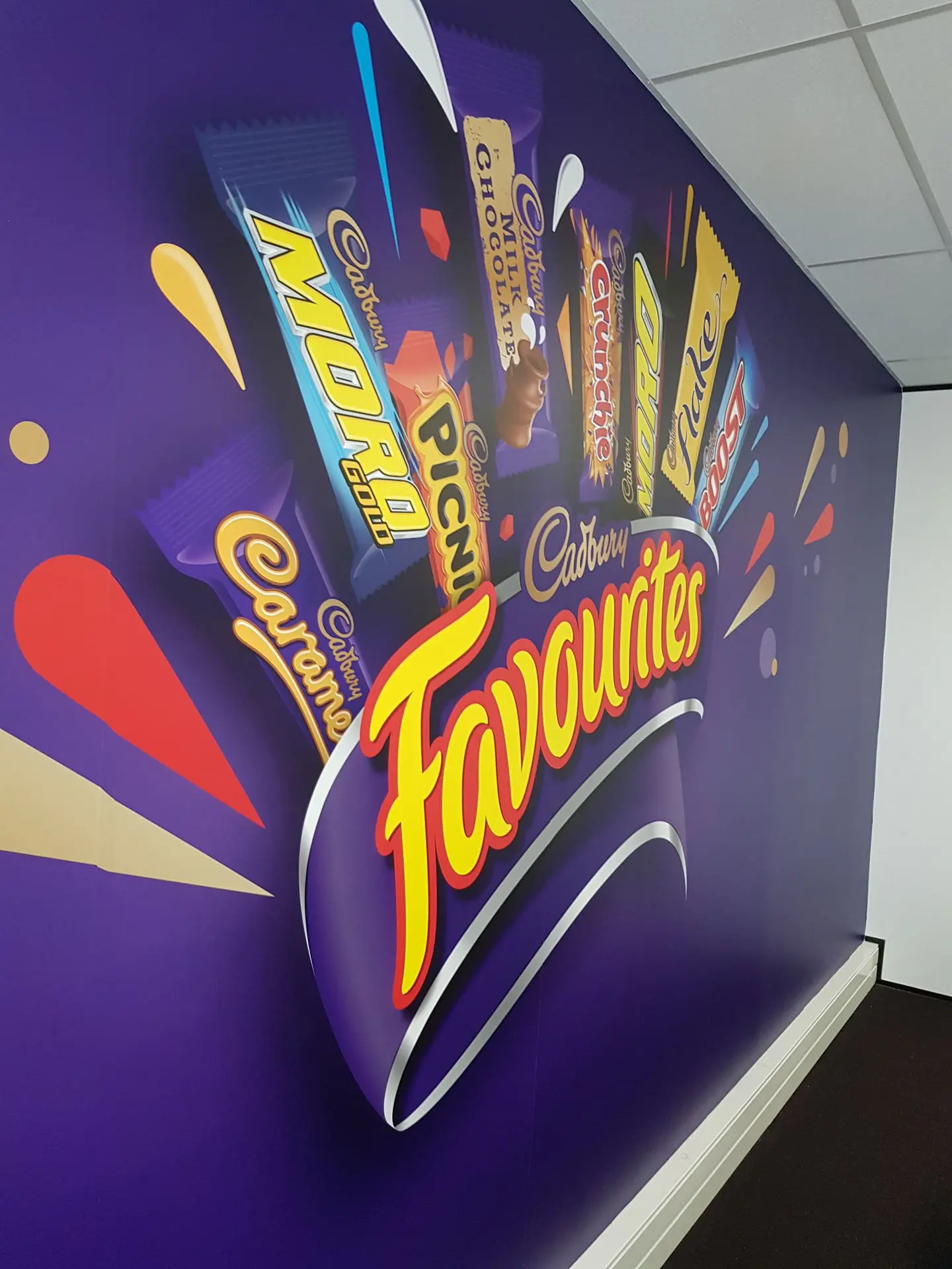 A bold floor to ceiling wall graphic features Cadbury chocolates branding for a meeting room space.